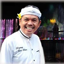 Dedi Mulyadi tersenyum mengenakan pakaian adat Sunda di depan latar air mancur warna-warni, dirinya viral karena usulkan vasektomi bagi suami.